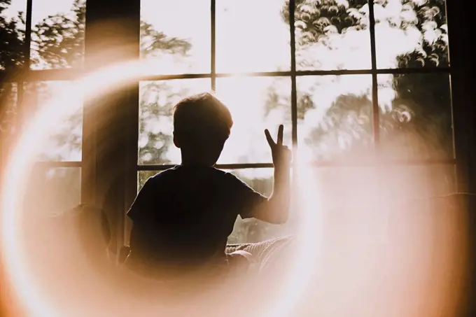 Back of Young Boy in Window Making Peace Sign With Circle Light Effect