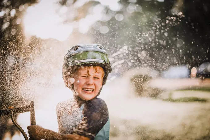 Young Boy Playing Outside in Sprinkler Splashing Water and Laughing