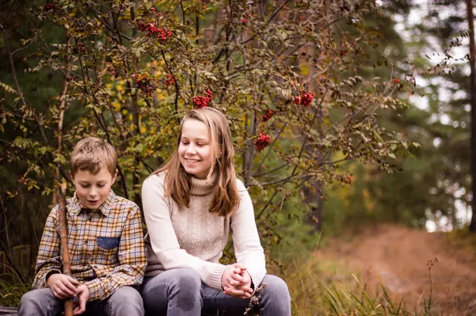 Two blond teenagers, a girl and a boy, a sister and a brother sit in the autumn forest and have fun chatting.