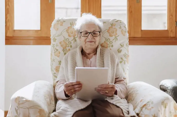 smiling elderly woman using a tablet on the sofa