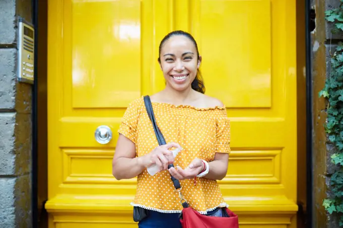 happy young hispanic woman applying sanitizer in the street