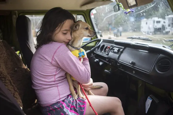 A girl hugs a chihuahua dog in VW camper van during roadtrip