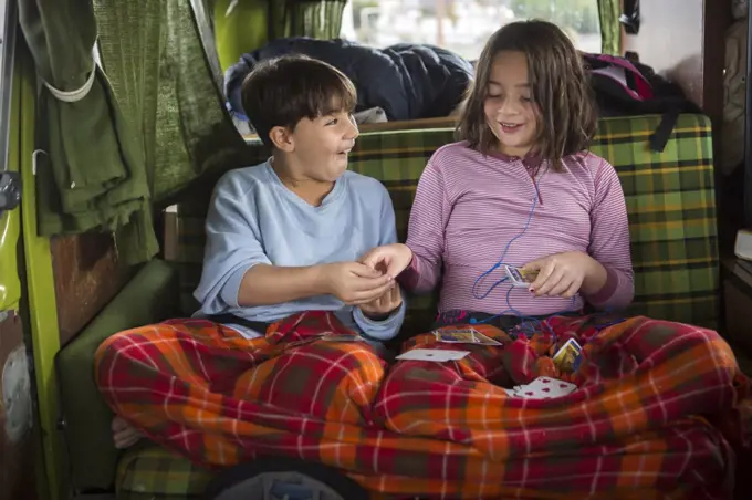 Brother and sister play cards in back of VW camper van during roadtrip