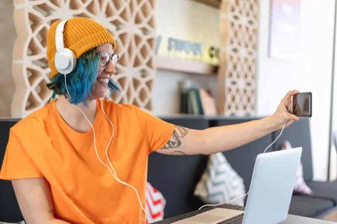 Modern young woman making selfie with smartphone and headphones