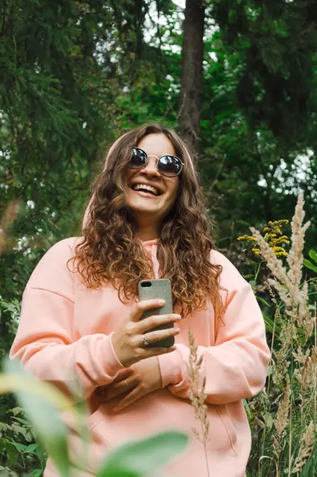 A young woman in a pink sweatshirt, in sunglasses, with a phone, laugh