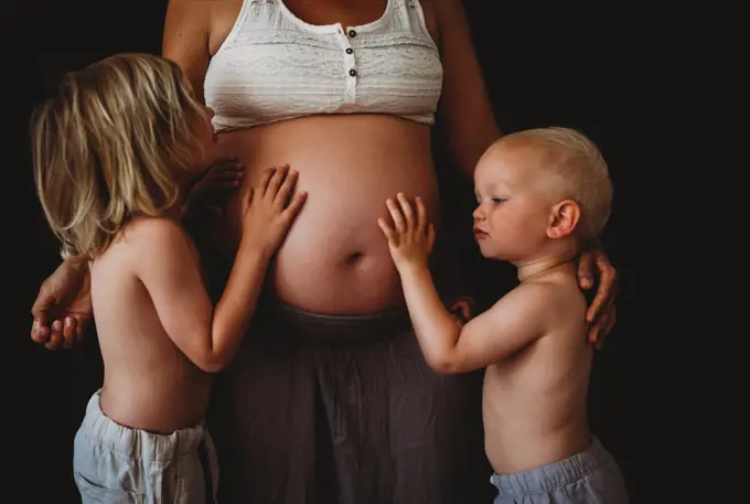 Young happy children hugging touching mom's pregnant big belly at home