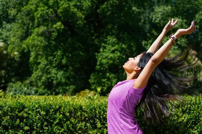 Young cheerful woman dancing outdoor. She is raising her arms on air.