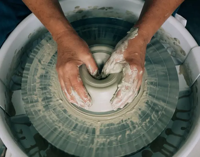 hands shaping pottery on a wheel with messy hands in a studio