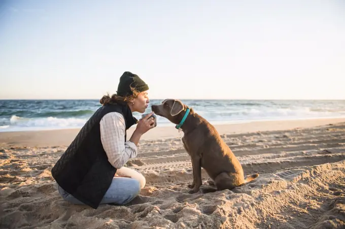 Young woman enjoying drink in mug while beach car camping with dog