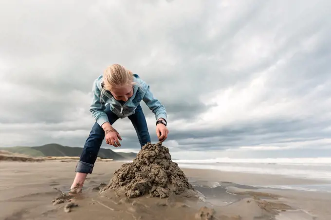 Tween building sand castle at beach in New Zealand on cloudy day