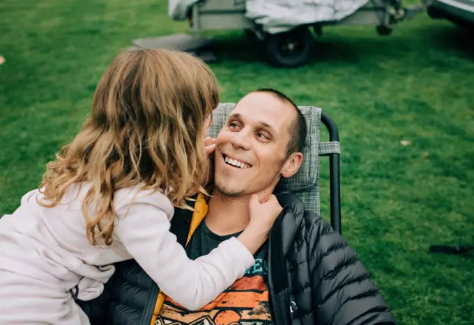 child playing with dads cheeks making him smile whilst camping