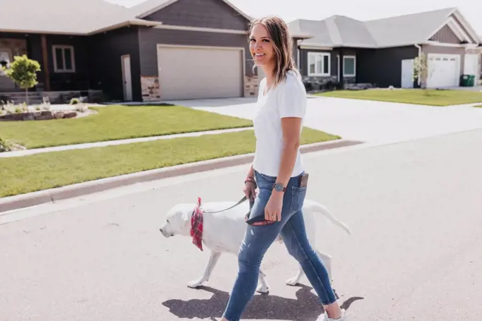 Woman walks dog through neighborhood on a sunny day