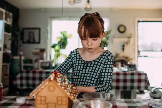 Young girl decorating a gingerbread house inside