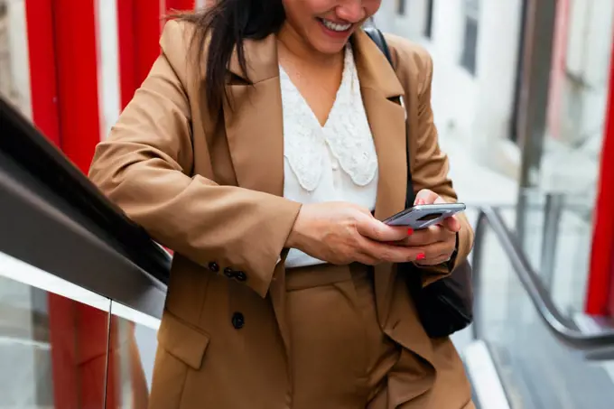 Crop business woman checking her cellphone on an escalator