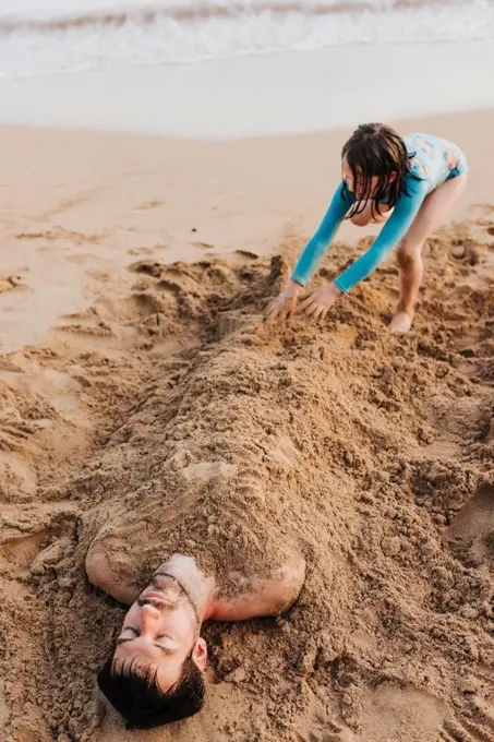 Daughter buries dad in the sand on Waikiki beach during sunset