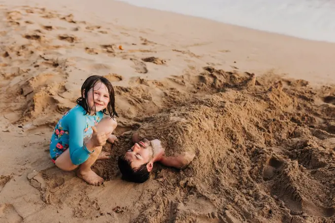 Young girl gives thumbs up after burying dad in sand on Waikiki beach