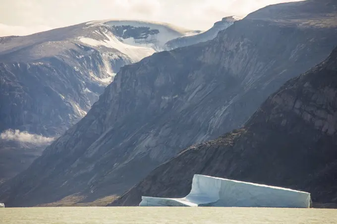 small iceberg floats in ocean below large sea cliffs