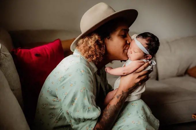 Black mother kissing her daughter on the couch.