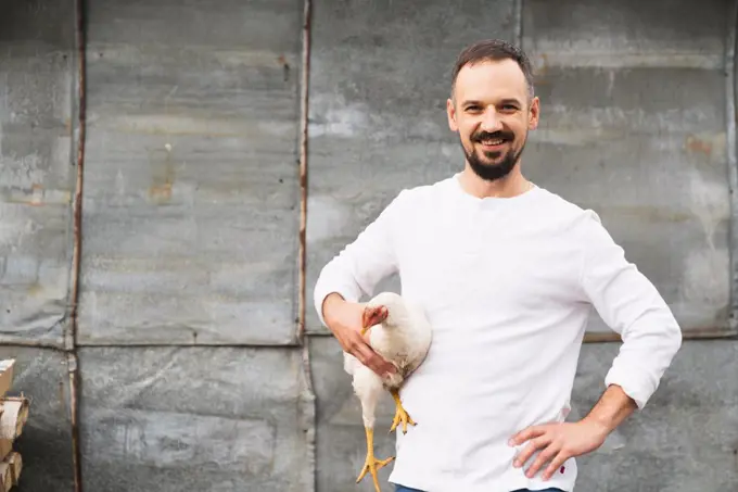 Portrait of farmer carrying chicken against grey wall