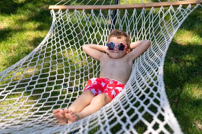 Silly boy relaxing on hammock in swimsuit and sunglasses