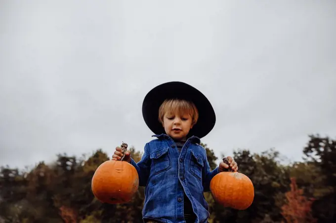 Boy wearing hat holding pumpkins in fall