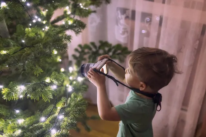 small toddler boy taking photos with camera of a christmass tree