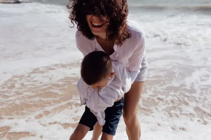 Young beautiful mommy playing with her baby son on the beach