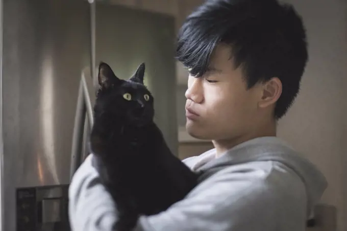 Asian teen boy in hoodie holds black cat