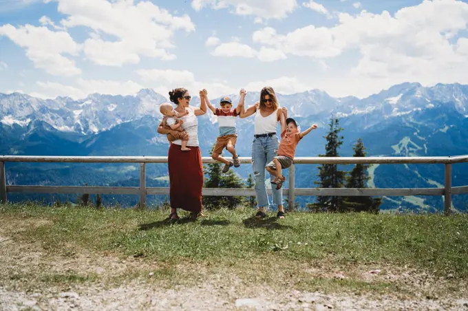 Kids jumping with two moms in mountains on sunny day