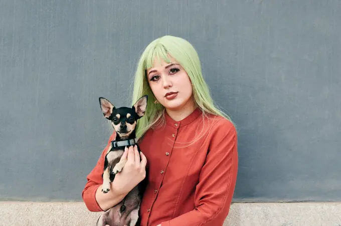 Alternative woman with green hair poses with her dog looking at camera