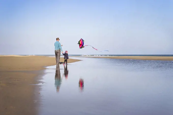 Father and daughter fly kite at beach in winter