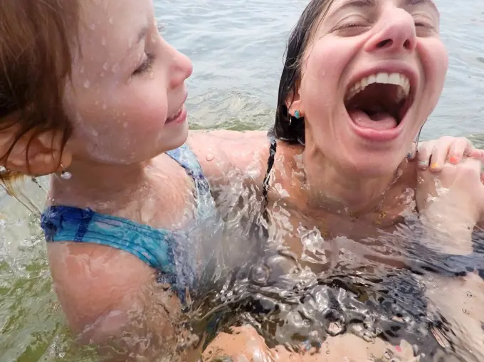 close up of mother and daughter laughing while in ocean together