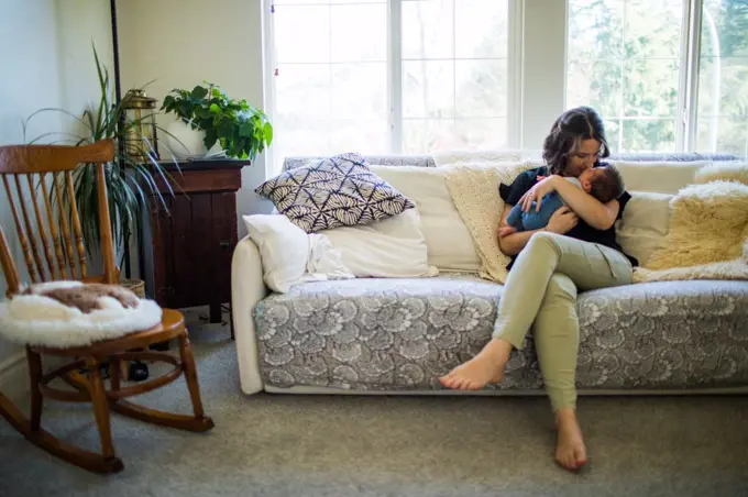 Loving mother embraces, kisses new newborn son at home.