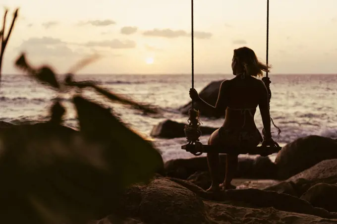 Silhouette of a happy girl swinging on a tropical beach surrounded