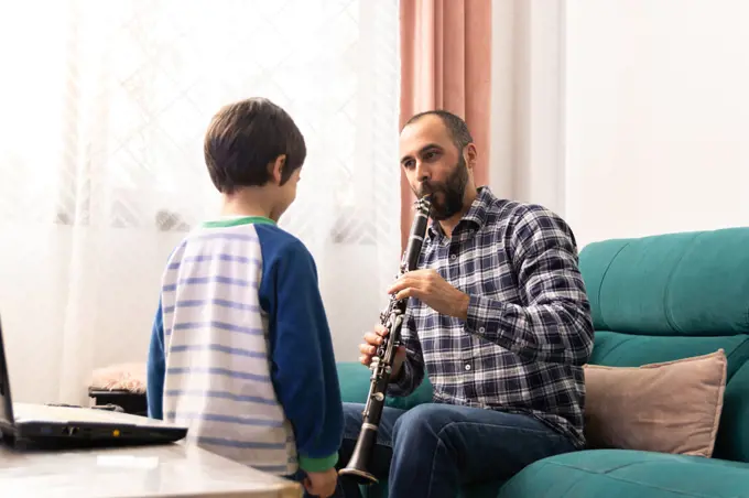 Father teaching his son to play the clarinet in the living room