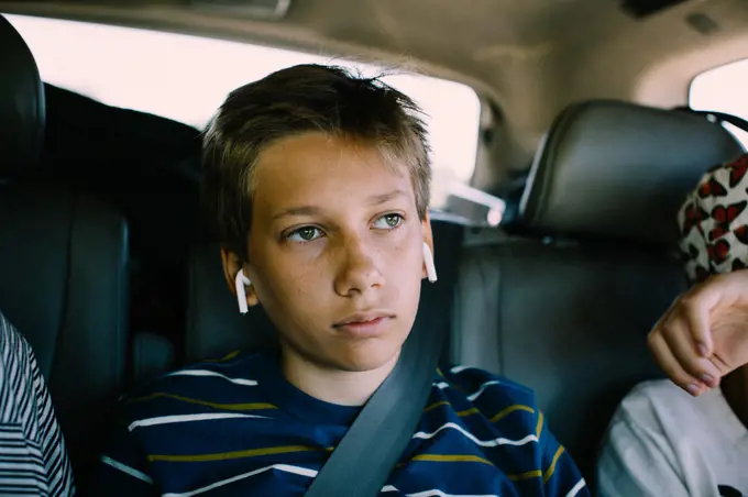 Bored Teen Boy Stuck in Backseat with Earphones on a Roadtrip