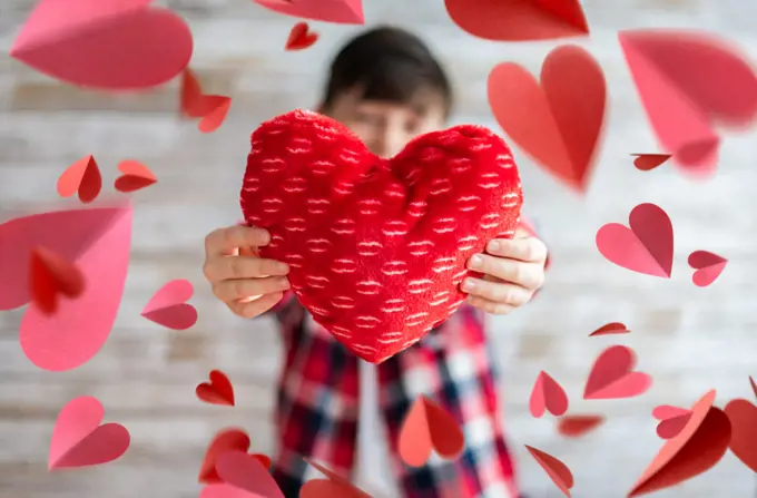 Boy holding heart pillow surrounded by floating paper hearts.