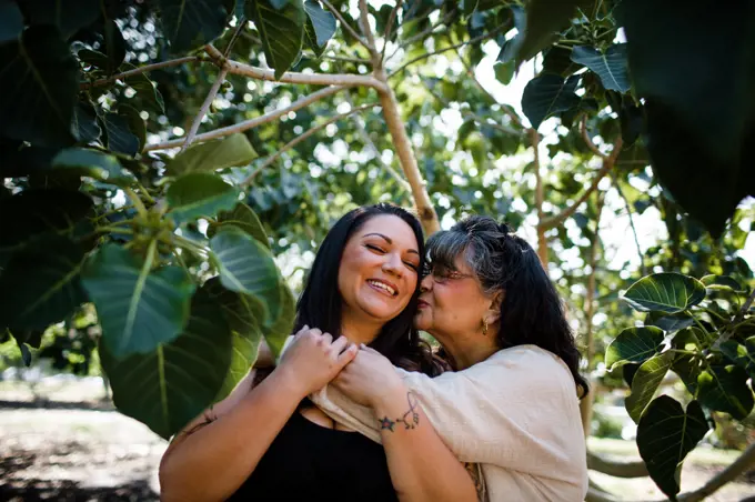 Mom Kissing Daughter at Park Surrounded by Trees in San Diego