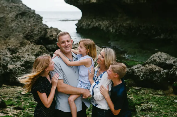 Family of five hugs and laughs together on tropical beach