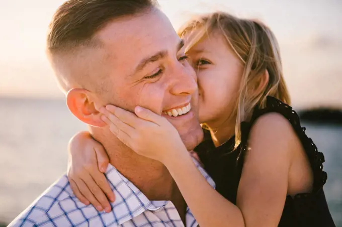 5 year old daughter gives father a kiss on the cheek by ocean