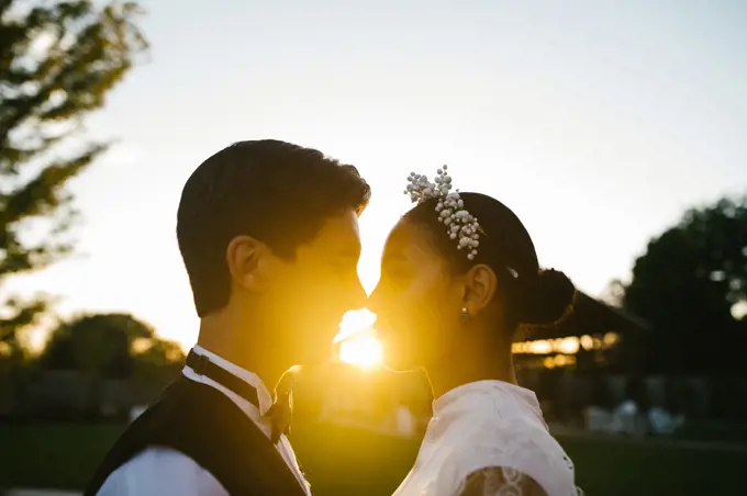 Multiracial couple touch noses in loving embrace with sunset