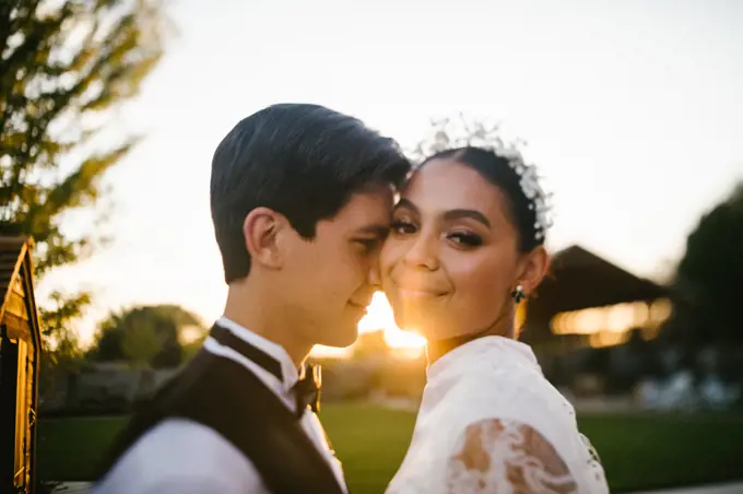 Bride and groom of mixed race snuggle in the sunset and golden light