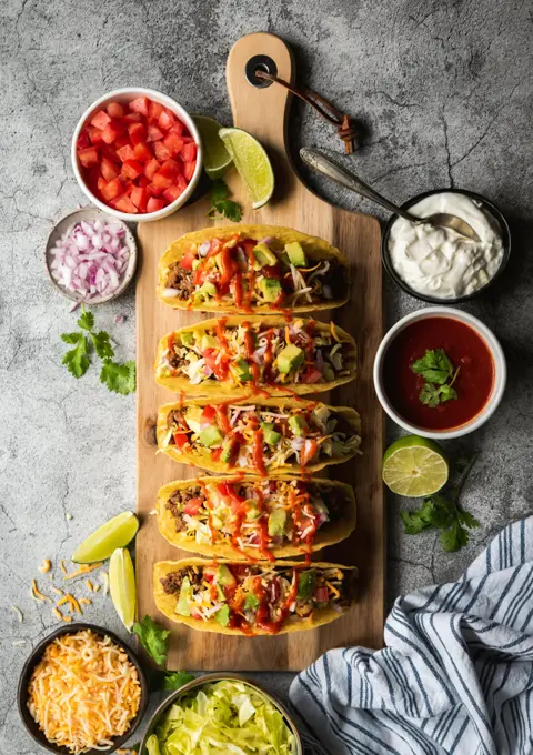 Hard shell tacos on wooden board with beef, lettuce, tomatoes, cheese.