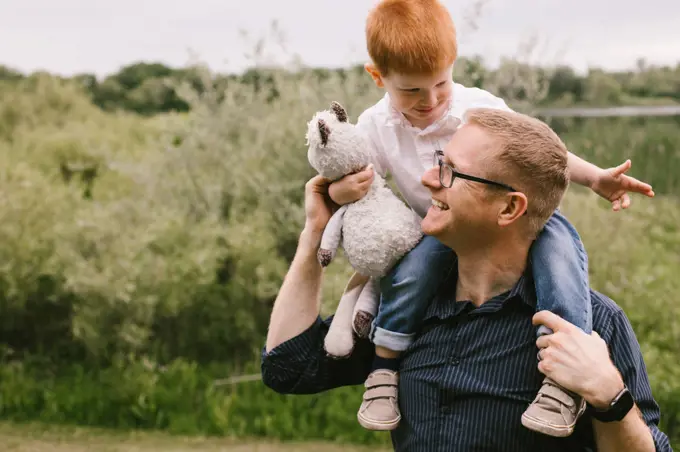 Son sits on dads shoulders while they smile and laugh