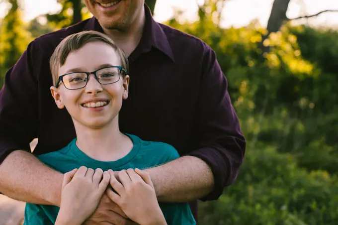 Preteen boy with glasses has happy smile while Dad hugs him