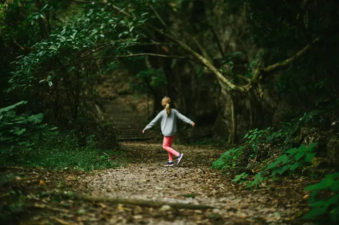 Girl child twirls on path in green forest