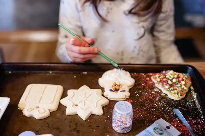 A child decorates a messy tray of Christmas cookies