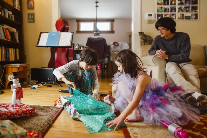 A father looks on while children open Christmas presents