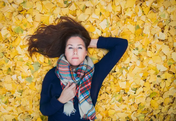 Portrait of a woman laying on a carpet of yellow leaves on autumn day.