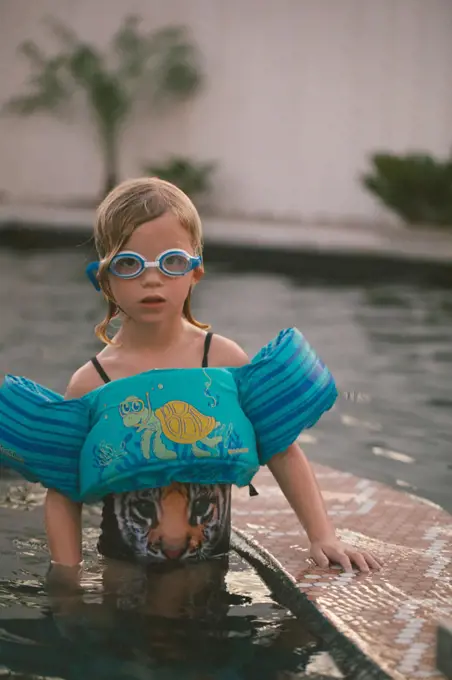 Child in floaty and goggles swimming in a pool in the evening